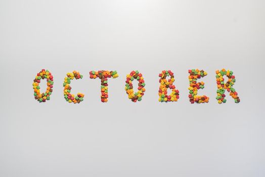October inscription on a white background. Confectionery sprinkles in the form of multi-colored maple leaves