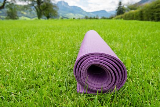 Rolled up fitness mat on the green grass background