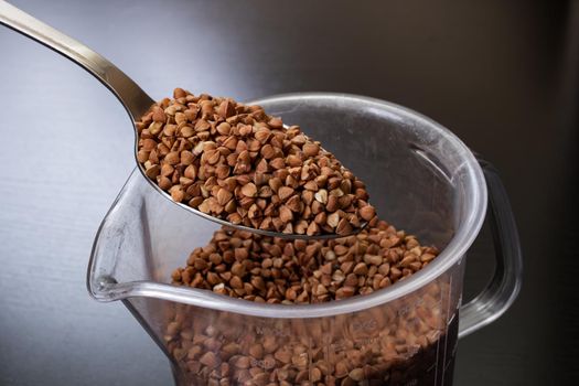 Buckwheat groats in a spoon on black background