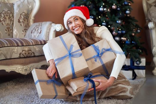 Christmas. Woman dressed white sweater Santa hat and jeans sitting on the floor near christmas tree with present box