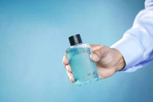 hand hold a mouthwash liquid container against blue background .