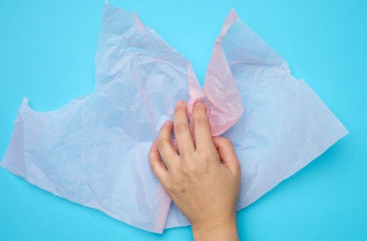 female hand hold pink folded wrapping crumpled paper on a blue background
