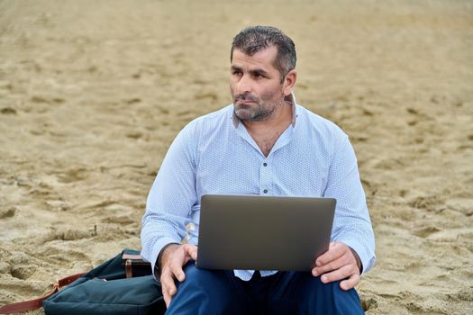 Serious confident mature man with laptop outdoors