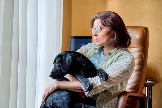 Portrait of middle aged woman and black labrador puppy dog