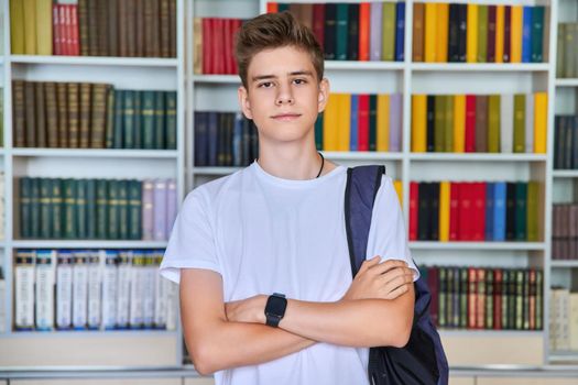 Single portrait of serious confident male student teenager looking at camera in library