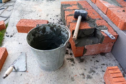 Bucket with a solute, trowel, rubber mallet and clay bricks