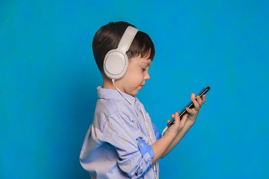 A boy with headphones on a blue background . Children's headphones. Harm of headphones for the child. Useful audiobooks for children. An article about children's leisure. Music.