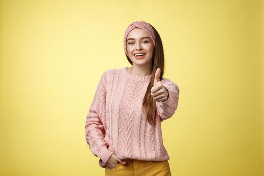 Gestures, emotions and lifestlyle concept. Self-assured positive 20s european woman wearing casual sweater over yellow background showing thumb up gesture, approving, accepting and liking concept