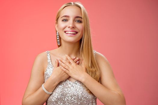 Grateful charming blond european 25s woman in silver party dress press palms heart feel thankful appreciate effort cherish romantic gesture receive flattering compliments gifts, smiling happily