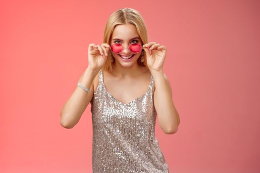 Lucky attractive stylish european blond female having fun friends nightclub wearing silver glittering dress sunglasses look amused curious peek camera intrigued, standing red background
