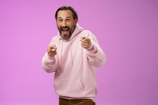 Gotcha. Portrait carefree funny amusing adult energized bearded man jumping pranking friend having fun laughing happily pointing camera index fingers greeting picking you, purple background