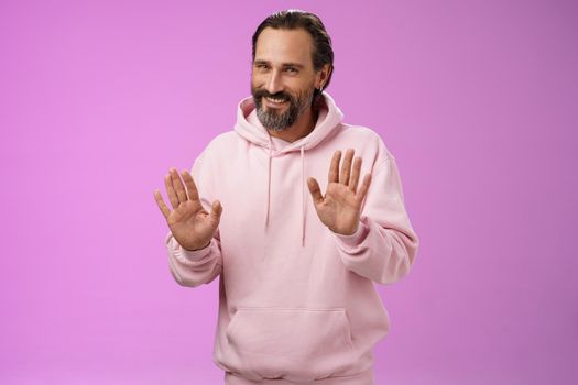 No thanks pass. Charming polite manly adult bearded man grey hair in pink hoodie apologizing refusal raise palms rejection gesture declining offer smiling say sorry not interested, purple background