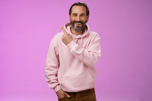 Charming friendly happy mature man 50s bearded grey hair laughing happily pointing upper left corner behind showing proudly family members standing purple background having fun stay positive