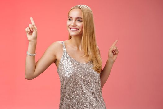 Carefree good-looking stylish glamour blond young 20s woman in silver glittering dress dancing having fun amused go wild party night prom shaking body raising index fingers up, red background