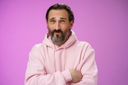 Unsure troubled caucasian bearded adult guy with earring pink hoodie press lips frowning counting mind standing hesitant doubtful thinking look up uncertain taking important decision