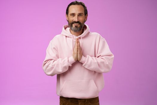 Peaceful attractive bearded mature mail model in trendy pink hoodie press palms together namaste praying gesture smiling delighted relaxed bowing buddhism faith, appreciating help, look thankful