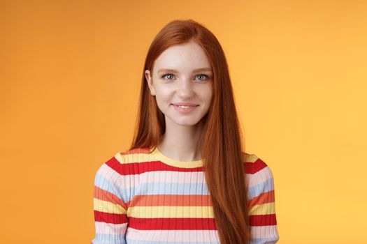 Pleasant friendly-looking confident smart redhead female student aim success smiling self-assured express lucky positive upbeat mood casually hang out orange background listening amusing story