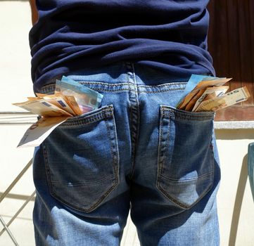 50 and 20 euro banknotes sticking out of the pockets of a blue jeans