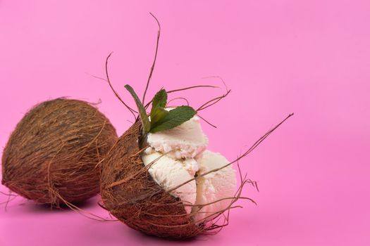 Vanilla ice cream balls in an empty coconut decorated with mint leaves on a pink background