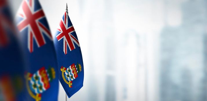 Small flags of Cayman Islands on a blurry background of the city