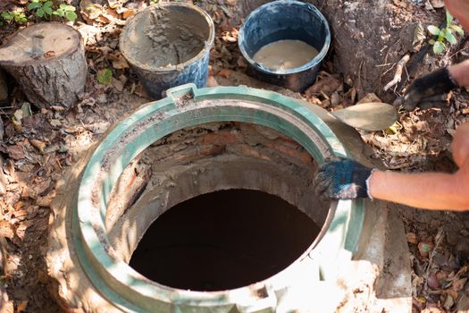 Laying a hatch on a sewer well. The man strengthens the neck of the septic tank