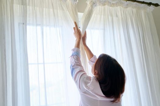 Close-up of woman's hand opening and closing light translucent curtains