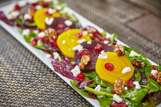 Colorful red and yellow beet salad with white feta cheese on a bed of greens on a long plate on a placemat foodie
