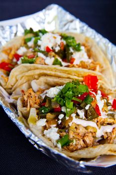 Delicious fresh tacos with chicken crema cilantro green onion and other vegetables in a foil lined paper holster