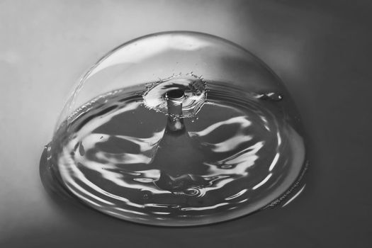 Black and white of pristine bubble containing ripples from two water drops colliding in air