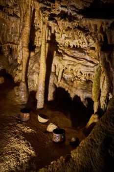 Old rusted drinking cups on ground of cave surrounded by stalagmites and stalactites
