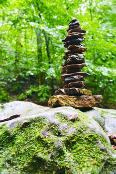 View of tall cairn stack of stones in woods on mossy boulder