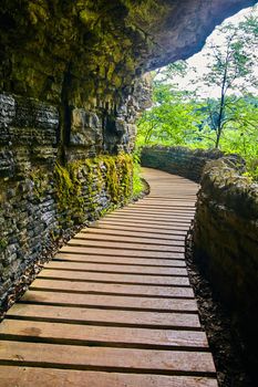 Peaceful wood boardwalk and stone wall against stone cliffs with moss and algae