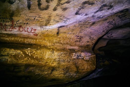 Names carved into cave wall surrounded in darkness