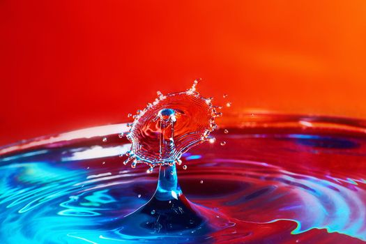 Two water drops colliding on blue water with red background