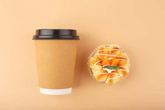Top view of coffee or tea in brown cardboard cup with pastry against beige background