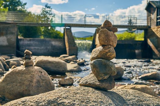 Stack of stones cairn next to dam river with walkway