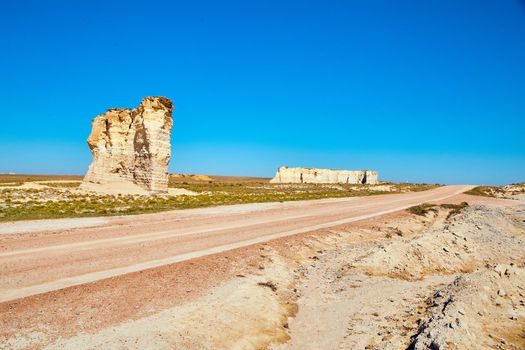 Dirt road through the flat desert with pillars of white rock