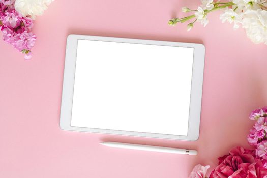 iPad pro tablet with white screen on pink color background with pen and flowers. Flatlay. Office background
