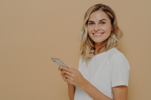 Portrait of cheerful young woman in white tshirt being happy to read good news on smartphone