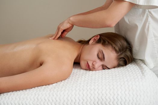 Masseur massaging young woman on massage table in a spa salon. Young woman relaxing during back massage at the spa. Spa treatment concept