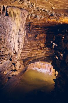 Waterfall in underground cave next to rock formations stalagmites and stalactites