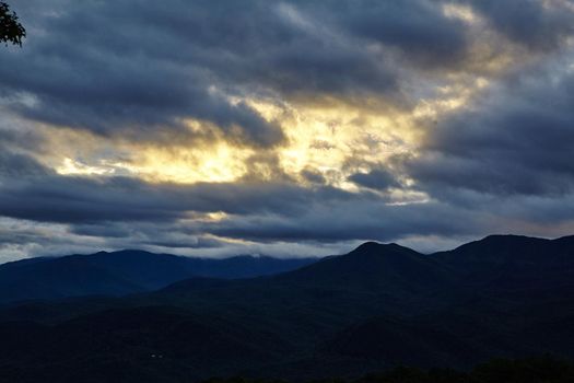 Smokey Mountains silhouetted against a dark cloudy sky with a streak of golden sunlight