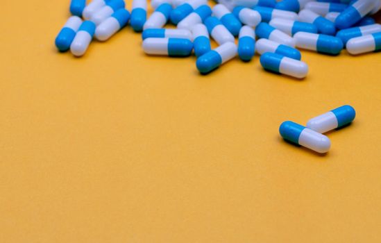Blue and white antibiotic capsule pills spread on yellow background. Antibiotic drug resistance. Antimicrobial drug. Pharmaceutical industry. Pharmaceutical products for pharmacy shop and hospital.