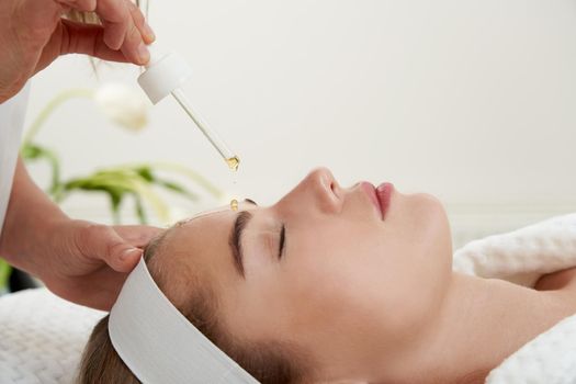 Face Skin Care. Closeup Of Beautiful Smiling Woman Receiving Serum Oil Treatment In Beauty Salon. Cosmetologist Applying Cosmetic Serum On female Face At Cosmetology Center