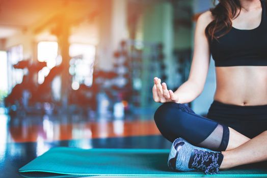 Woman doing yoga on mat at fitness gym. Sport and Exercise concept. Meditation and Fitness theme. Selective focus on hand