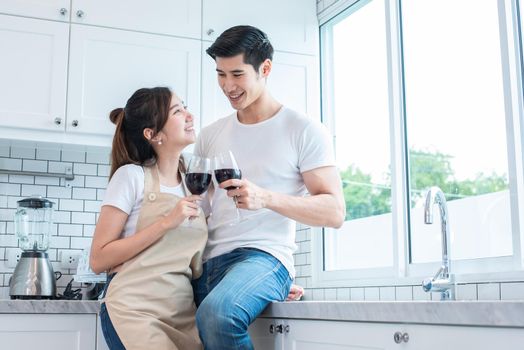 Asian lovers or couples drinking wine in kitchen room at home. Love and happiness concept. Sweet honeymoon and Valentine day theme