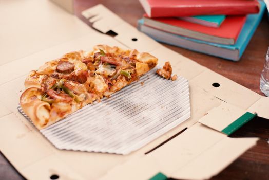 Piece of Pizza on table. Pizza on table with books and drinks for students who celebrating party after examination. Cut off pizza in delivery box. Food and beverage concept. Park and outdoors theme