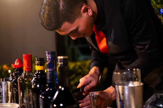 Professional bartender preparing fresh juice cocktail in drinking wine glass with ice at night bar clubbing counter. Occupation and people lifestyles concept. Outdoor and nightclub background