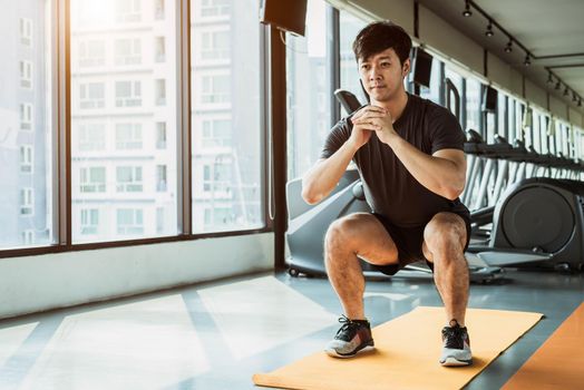 Sport man doing squat posture on yoga mat in fitness gym at condominium in urban. People lifestyles and Sport workout concept.