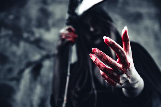 Witch showing bloody hand. Female demon angel in black clothes and hood on grunge wall background. Halloween day and Mystery concept. Fantasy of magic theme. Afterlife and Death concept.